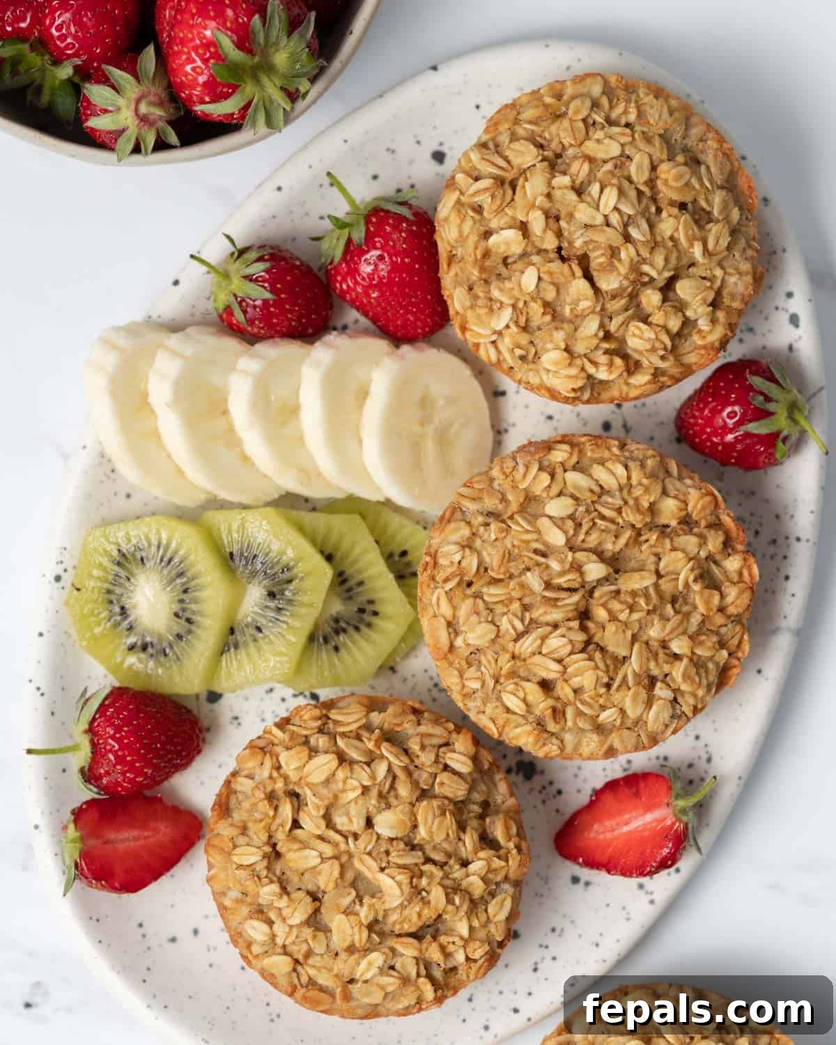 Three protein muffins neatly arranged on a plate, accompanied by a colorful side of sliced fresh fruits.