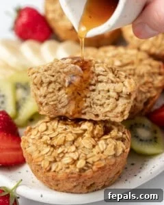 Maple syrup being added over half of a muffin stacked over another whole muffin on a plate