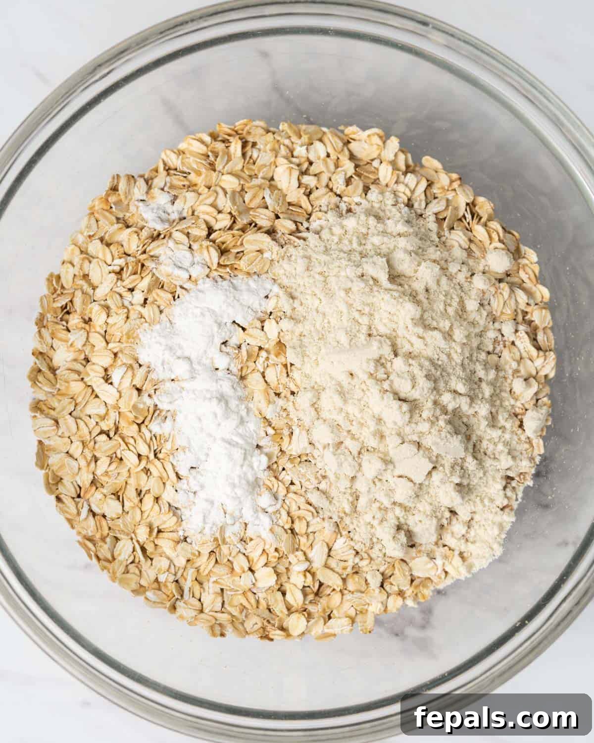 Rolled oats, baking powder, and protein powder are combined in a large round mixing bowl.