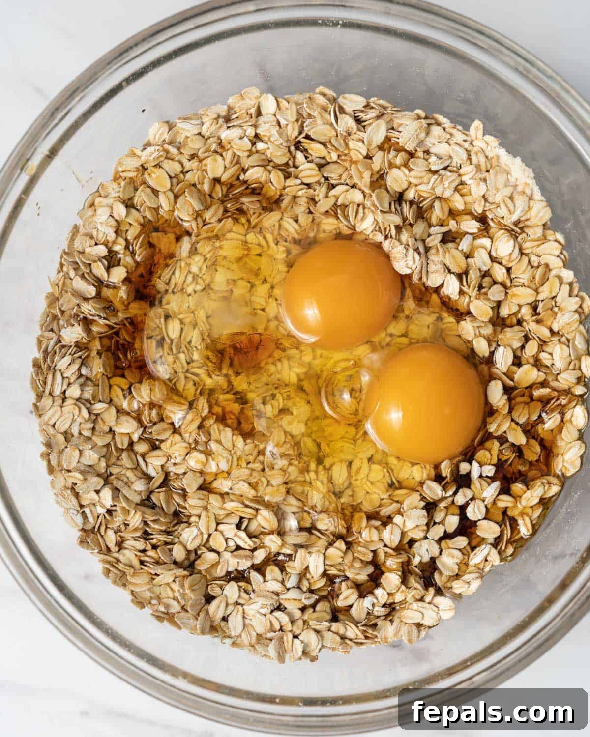 Milk, eggs, and maple syrup are poured into the oat mixture in a mixing bowl, ready for combining.