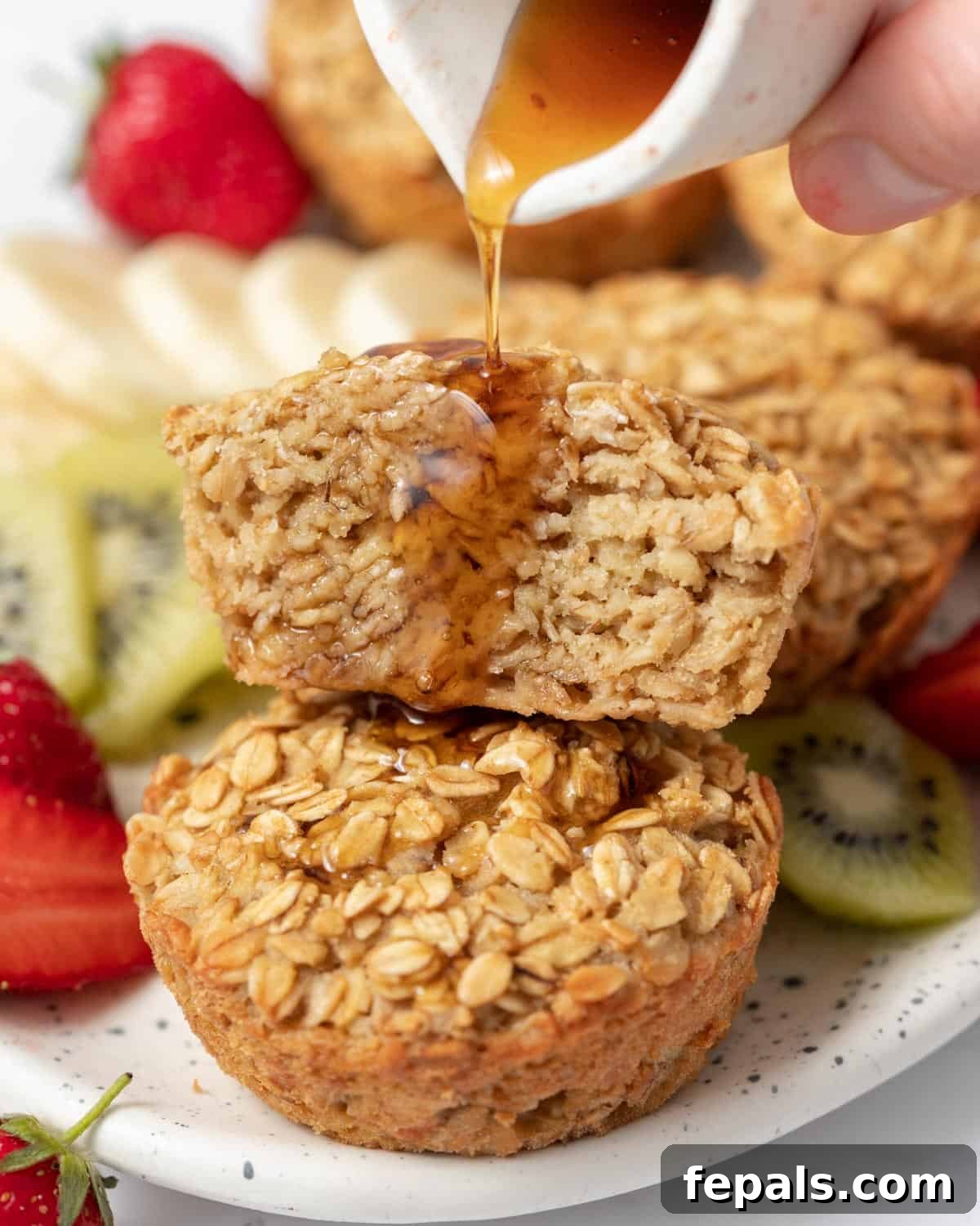 A stream of maple syrup drizzles over half a muffin, which is delicately stacked atop a whole muffin on a serving plate.