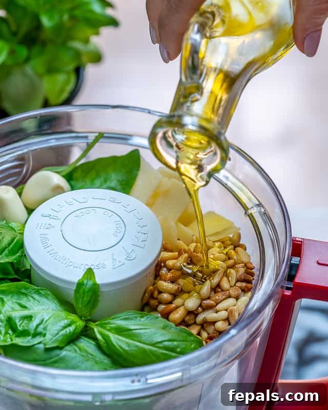 Garden Fresh Pesto Bliss 5 olive oil being added into the food process base with all the other ingredients to make homemade pesto