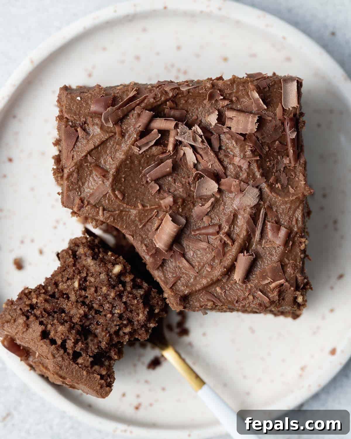 Velvety Chocolate Zucchini Indulgence 8 a single square piece of chocolate cake topped with frosting with a spoon cutting a bite off.