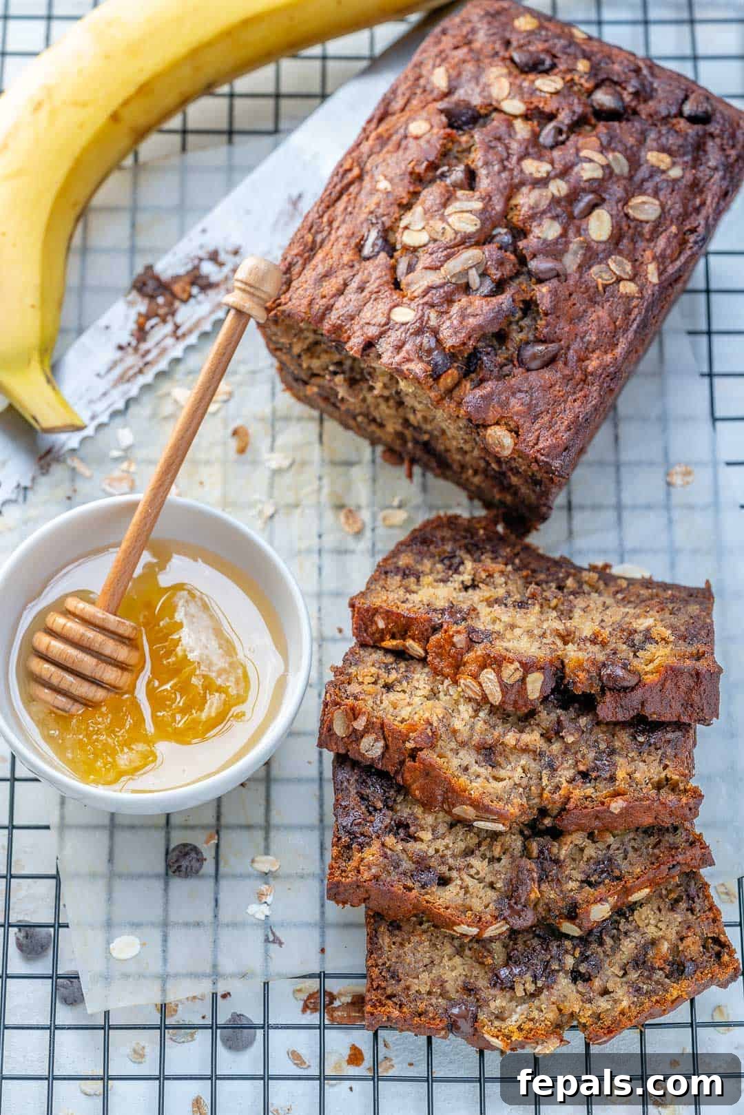 Two slices of healthy chocolate chip banana bread on a wire rack, with a bowl of honey beside them.