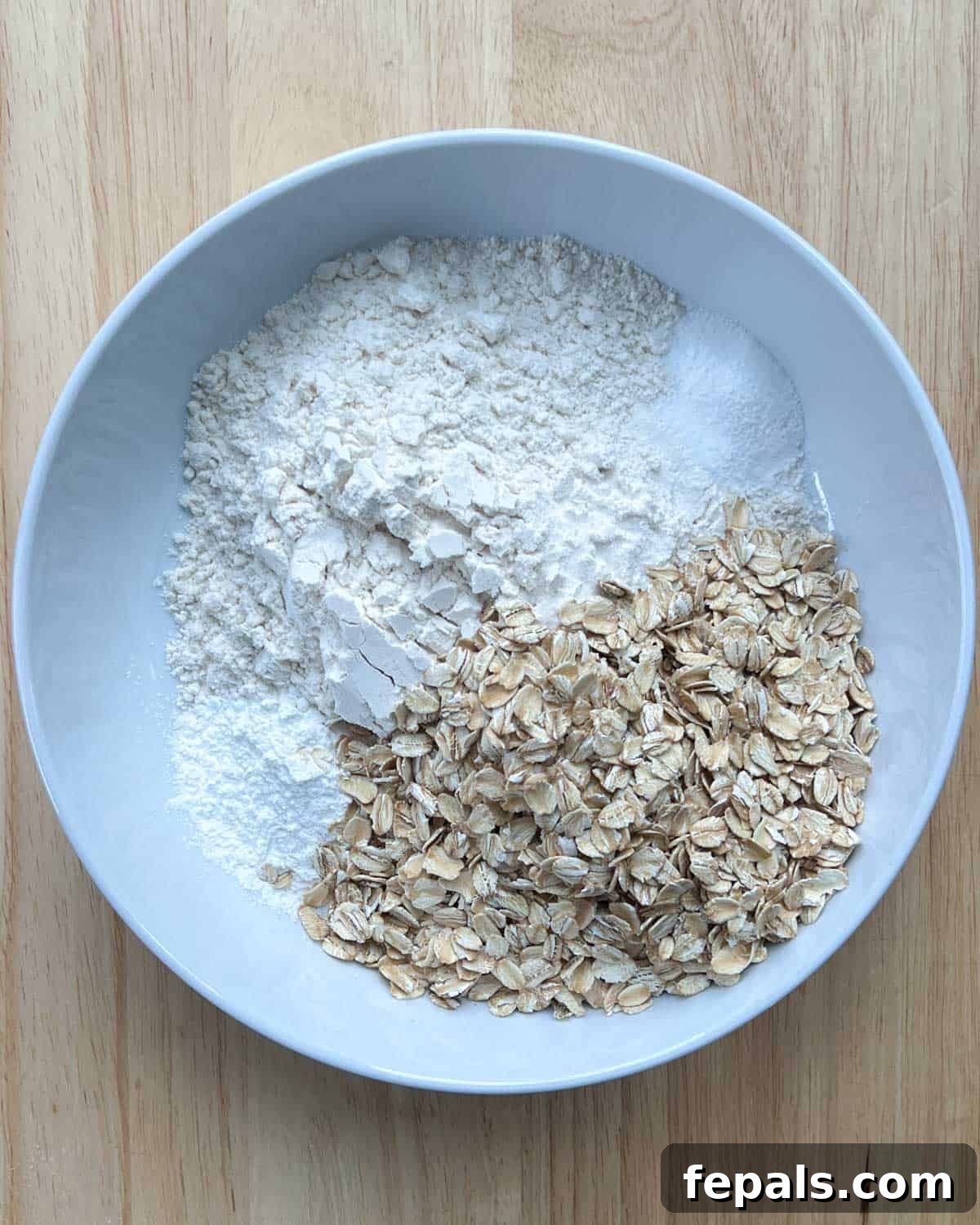 A round bowl containing flour, oats, baking powder, and baking soda, ready to be mixed.