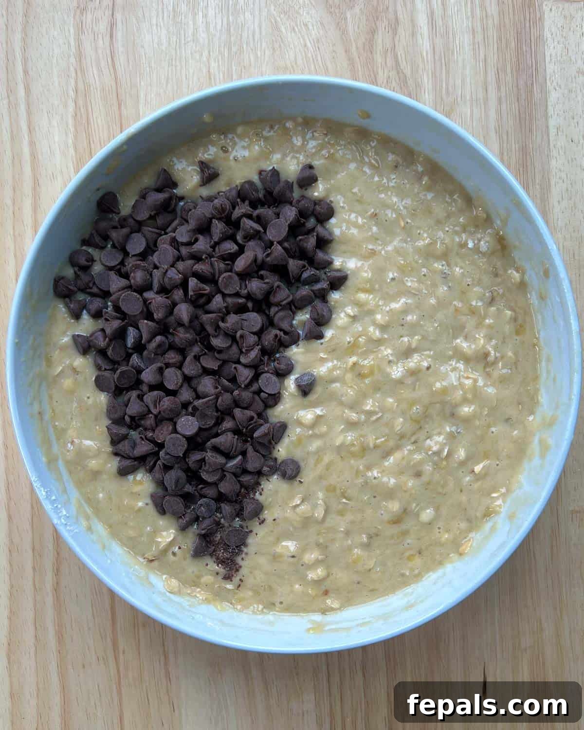 Dark chocolate chips being added to the banana bread batter in a round bowl, ready for mixing.