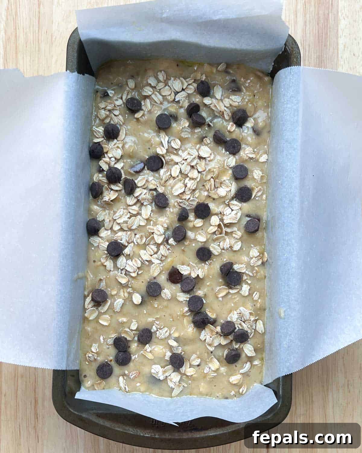 Banana bread batter in a loaf pan, topped with extra chocolate chips and oats before baking.