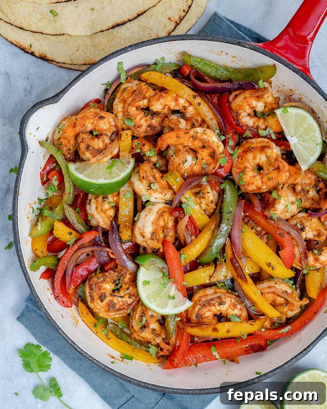 Sizzling shrimp fajitas in a skillet with colorful bell peppers and onions, garnished with fresh cilantro, ready to be served with tortillas.