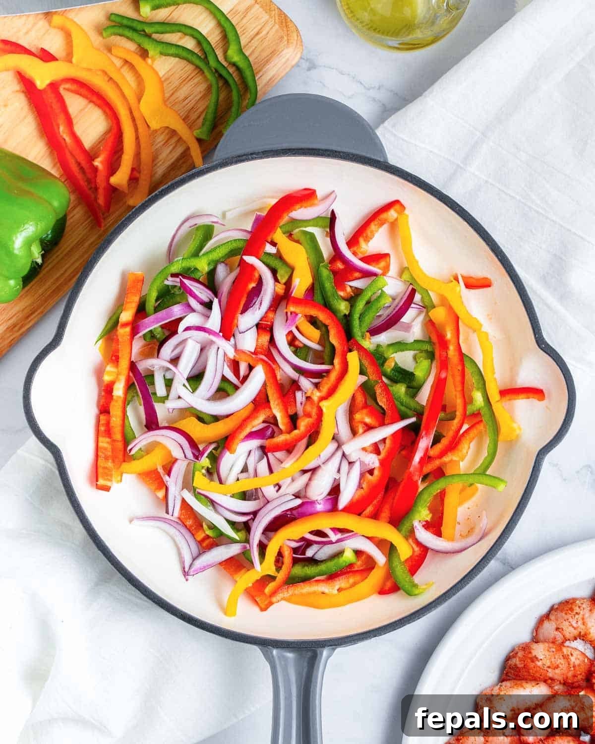 Thinly sliced bell peppers and red onions beginning to sizzle in a hot cast-iron skillet with olive oil.