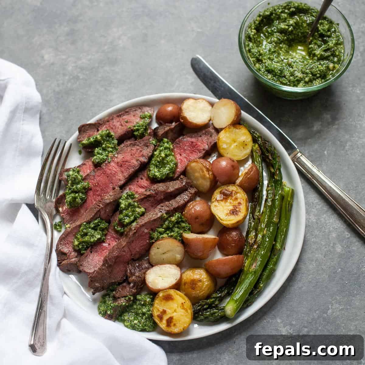 Sheet Pan Steakhouse Dinner 3 Sheet Pan Steak on white plate with utensils and kale pesto, showing a close-up of the meal.