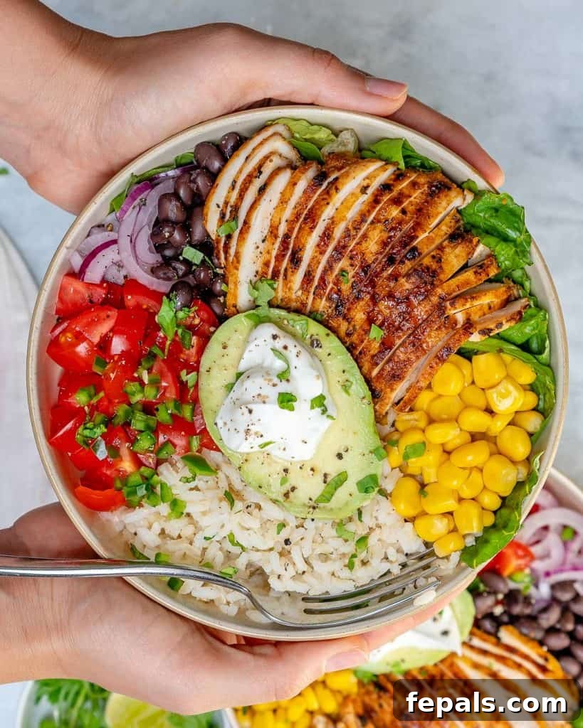 Fiesta Chicken Bowl 2 Top view of a hand holding a bowl of Grilled Chicken Burrito Bowl, showcasing grilled chicken, corn, beans, avocado, and lime.