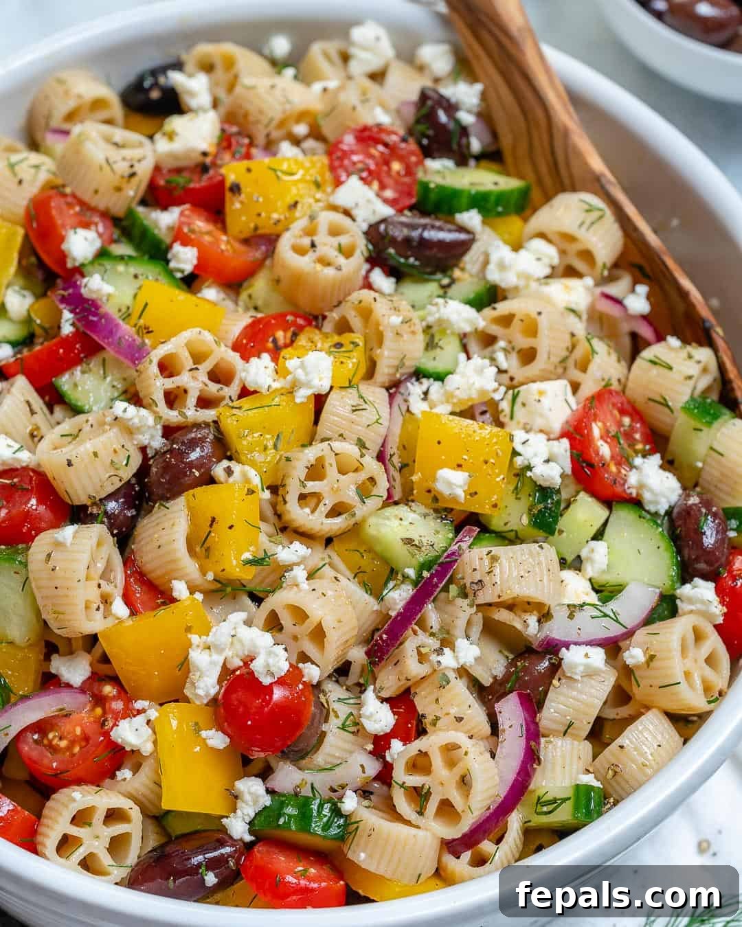 Zesty Greek Pasta Salad 5 A close-up shot of a colorful pasta and vegetable salad, generously studded with feta cheese, in a simple white bowl.