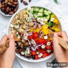 Zesty Greek Pasta Salad 7 hand mixing salad with a wooden spoon and fork in a round bowl.