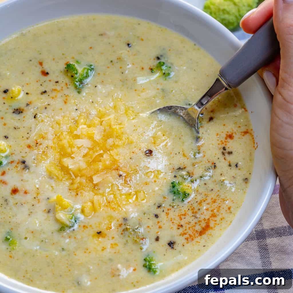 Wholesome Broccoli Cheddar Bliss 3 hand holding spoon in a bowl of Broccoli Cheddar Soup recipe topped with shredded cheese
