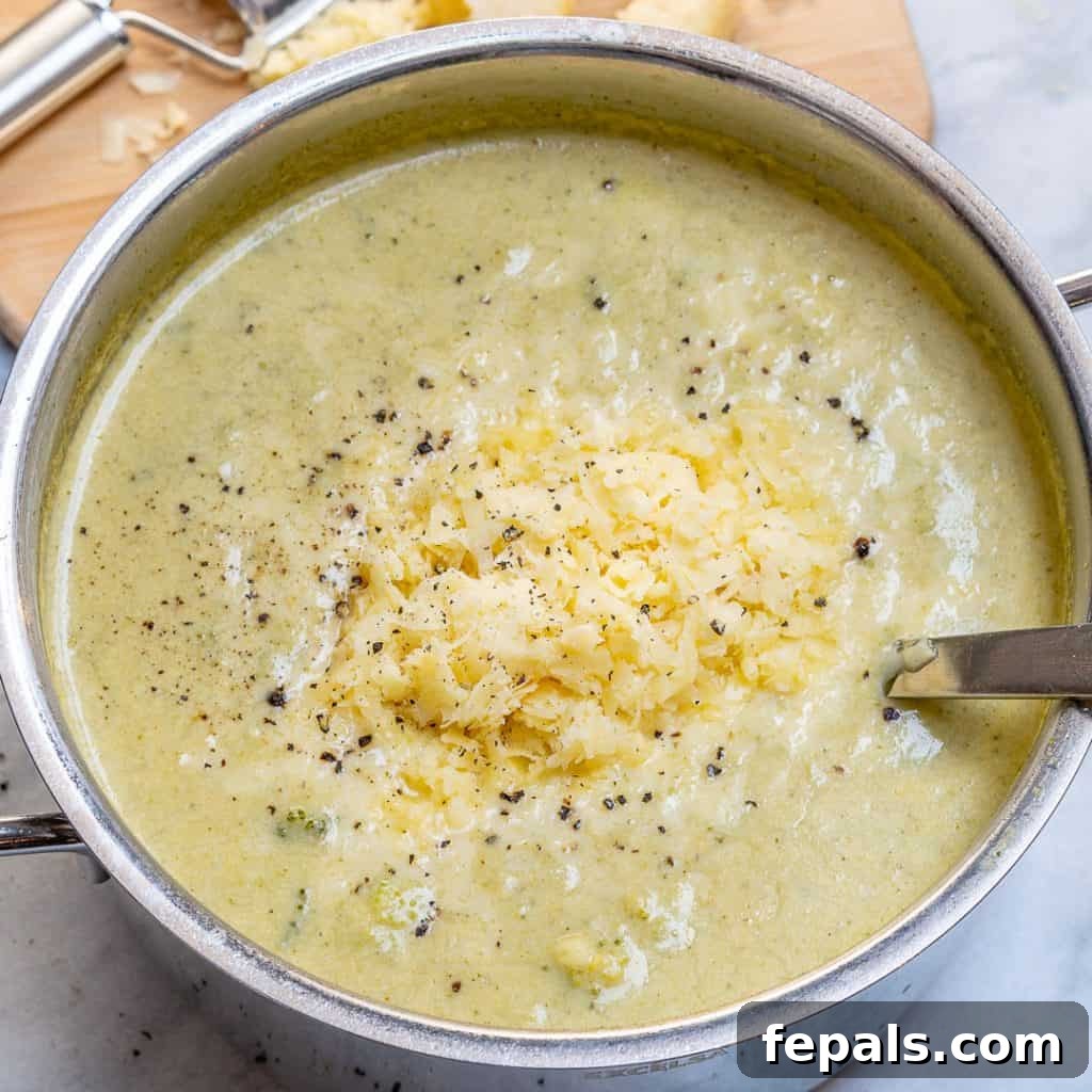 Wholesome Broccoli Cheddar Bliss 5 shredded cheese added over creamy broccoli soup in a pot with spoon in pot