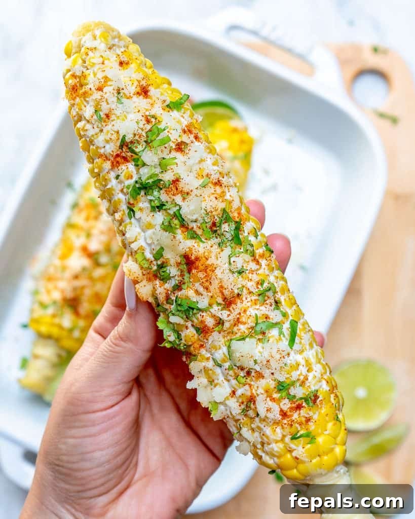 Effortless Elote 3 hand holding a single corn on the cob topped with crumbled cheese