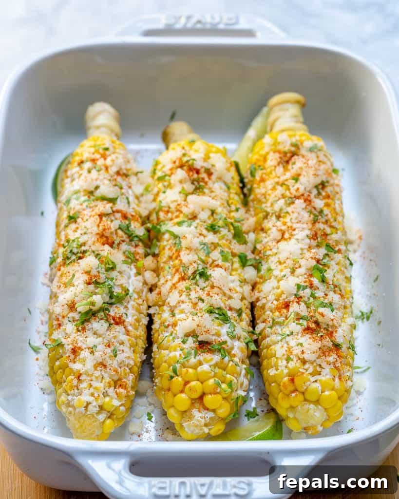 Effortless Elote 4 side shot of a white dish with 3 corn on the cob topped with crumbled cheese and cilantro