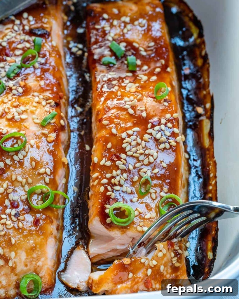 Sticky Teriyaki Salmon Bake 5 Fork flaking a piece of baked teriyaki salmon, showing its tender texture, garnished with sesame seeds and sliced green onions