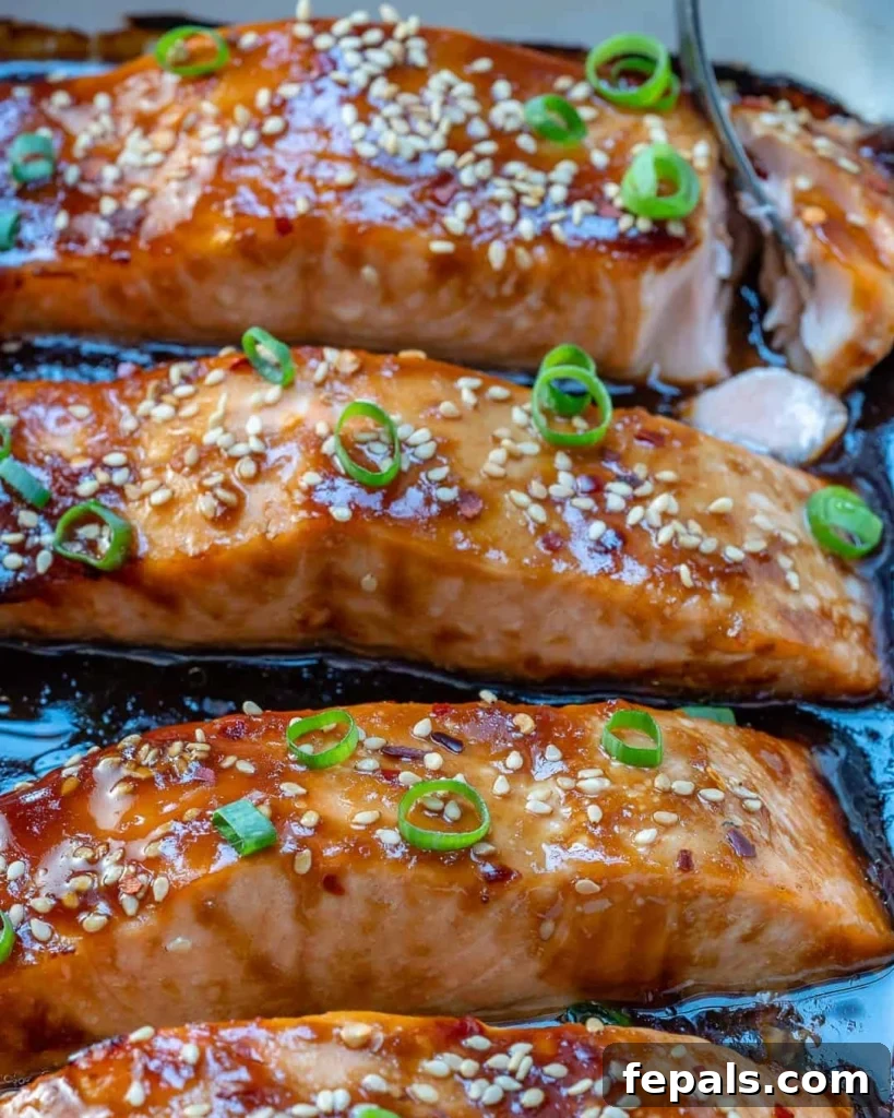 Sticky Teriyaki Salmon Bake 6 Side view of three baked teriyaki salmon fillets in a white dish, garnished with sesame seeds