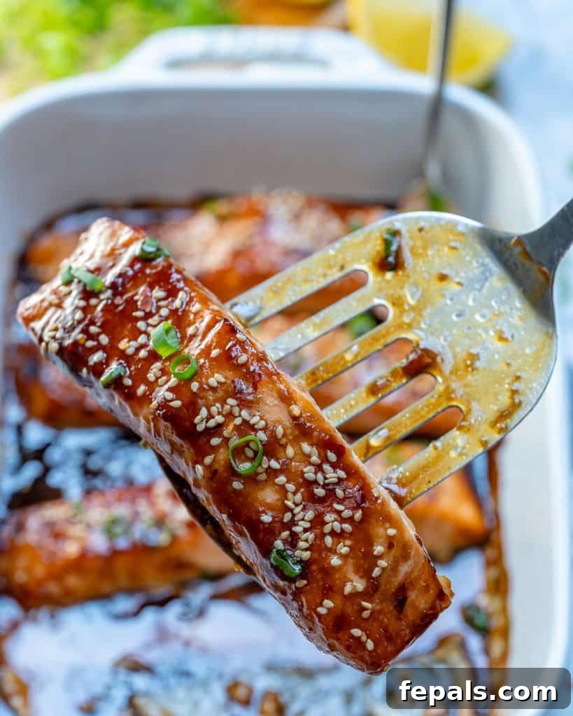 Sticky Teriyaki Salmon Bake 7 Metal spatula holding a piece of baked teriyaki salmon, garnished with sesame seeds and sliced green onions, ready to be served