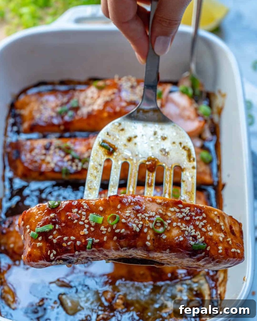 Sticky Teriyaki Salmon Bake 9 Spatula holding a baked teriyaki salmon fillet garnished with sesame seeds and green onions