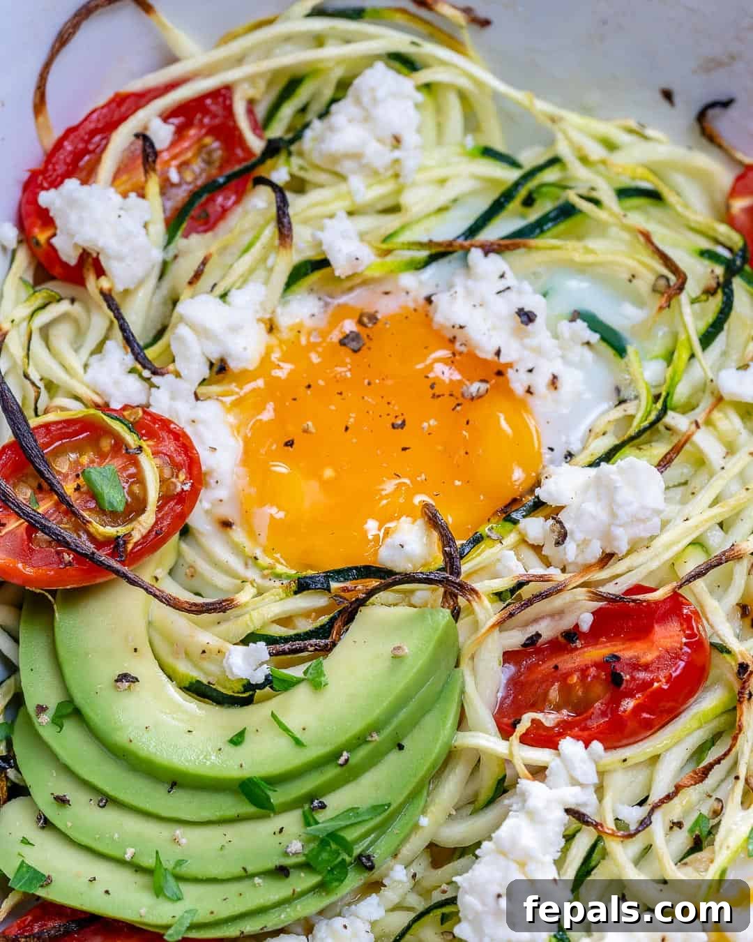 Baked egg in a dish with zoodles and sliced avocado.