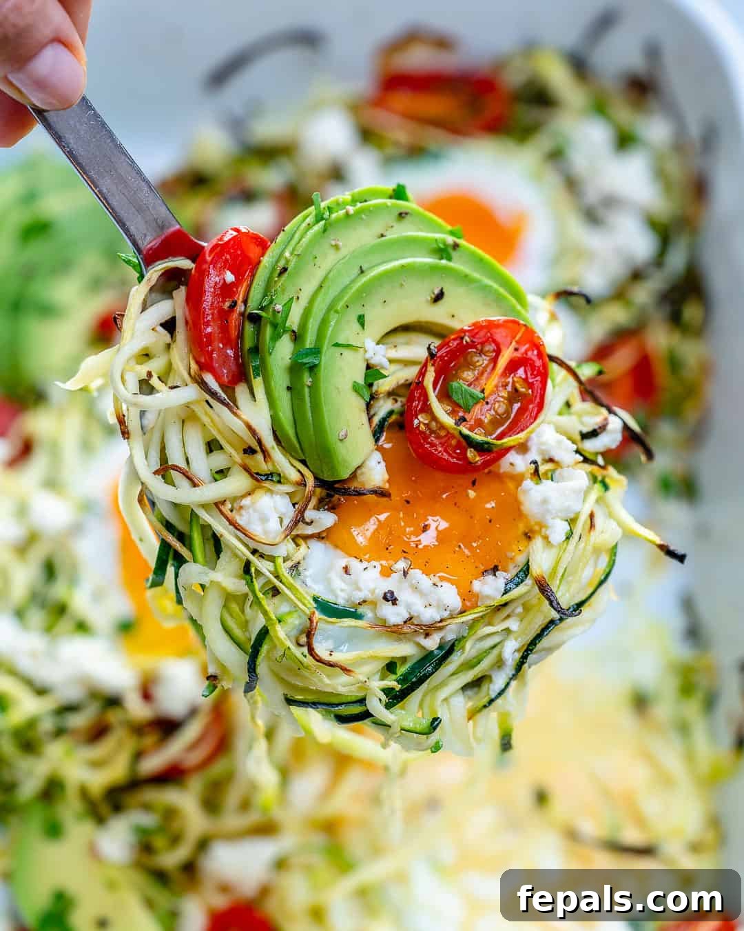 Hand holding spatula with a portion of baked zoodles and eggs.