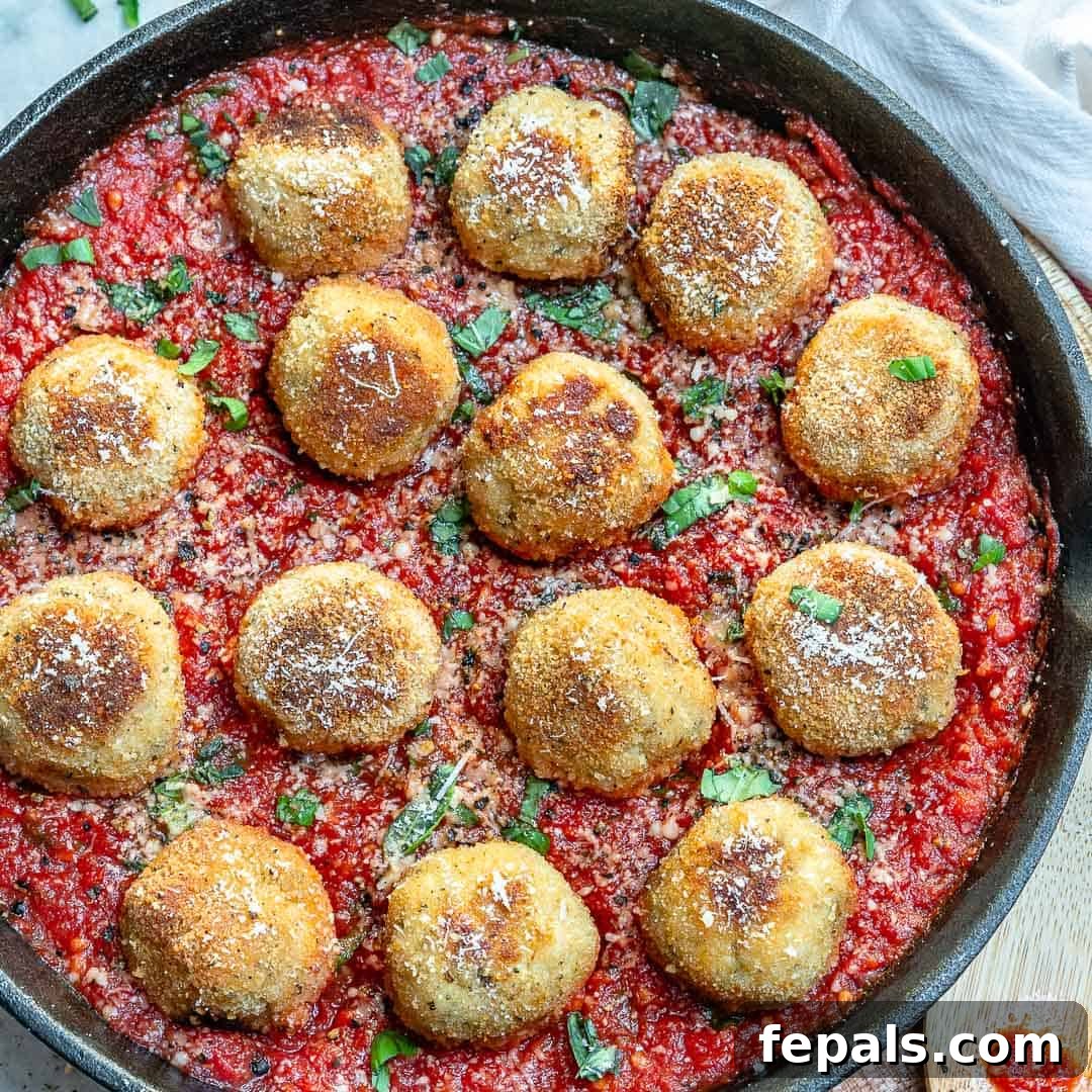 Cheesy Chicken Parmesan Meatballs with Tomato Garlic Sauce A large skillet filled with simmering garlic tomato sauce, with a few chicken parmesan meatballs visible within the sauce.