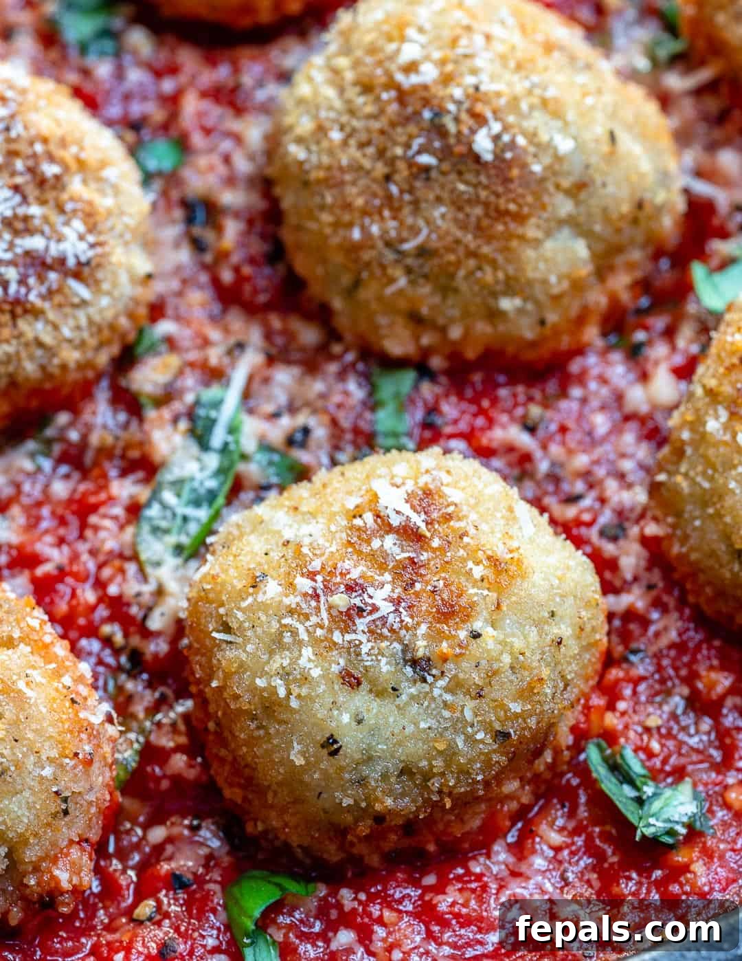 Easy Chicken Parmesan Meatballs in Tomato Sauce Close-up Close-up view of a single chicken parmesan meatball, cheesy and perfectly cooked, with a spoon of rich tomato sauce.