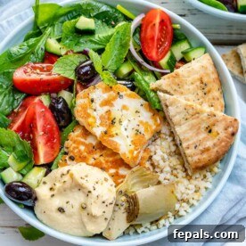 a round Mezze bowl with greens, grilled halloumi, hummus, and pita.