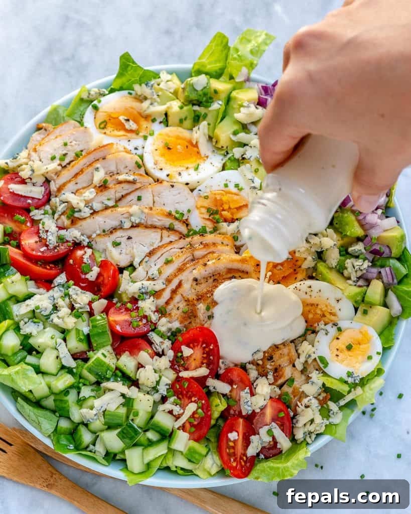 hand holding dressing jar and pouring it over salad 