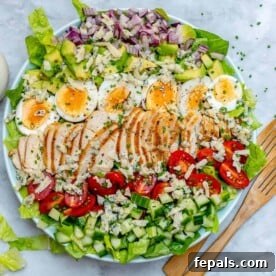 top view of a round bowl with chicken cobb salad and wooden serving spoon next to it