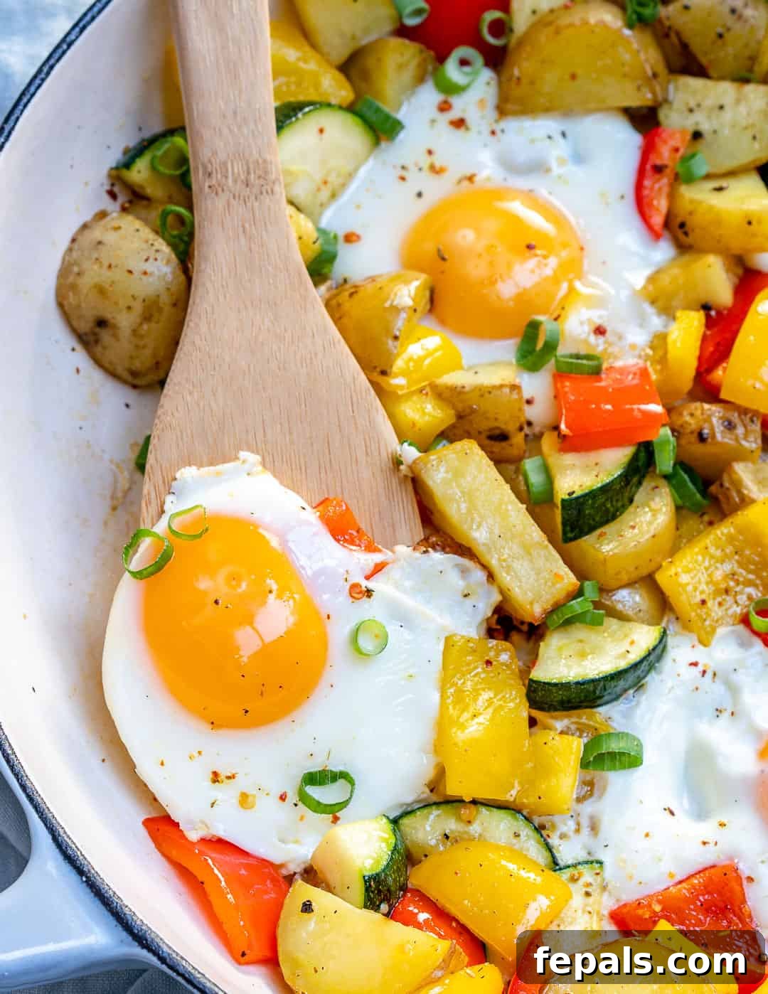 Sunrise Skillet with Eggs and Garden Harvest 2 A beautifully cooked egg and veggie breakfast skillet, featuring sunny-side-up eggs, vibrant potatoes, zucchini, and bell peppers, with a wooden spoon resting in the pan, ready to be served.