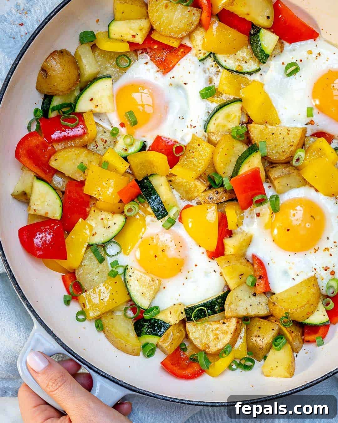 Sunrise Skillet with Eggs and Garden Harvest 4 A hand holding a skillet filled with a freshly cooked one-pan egg and veggie breakfast, highlighting the ease of preparation and serving.