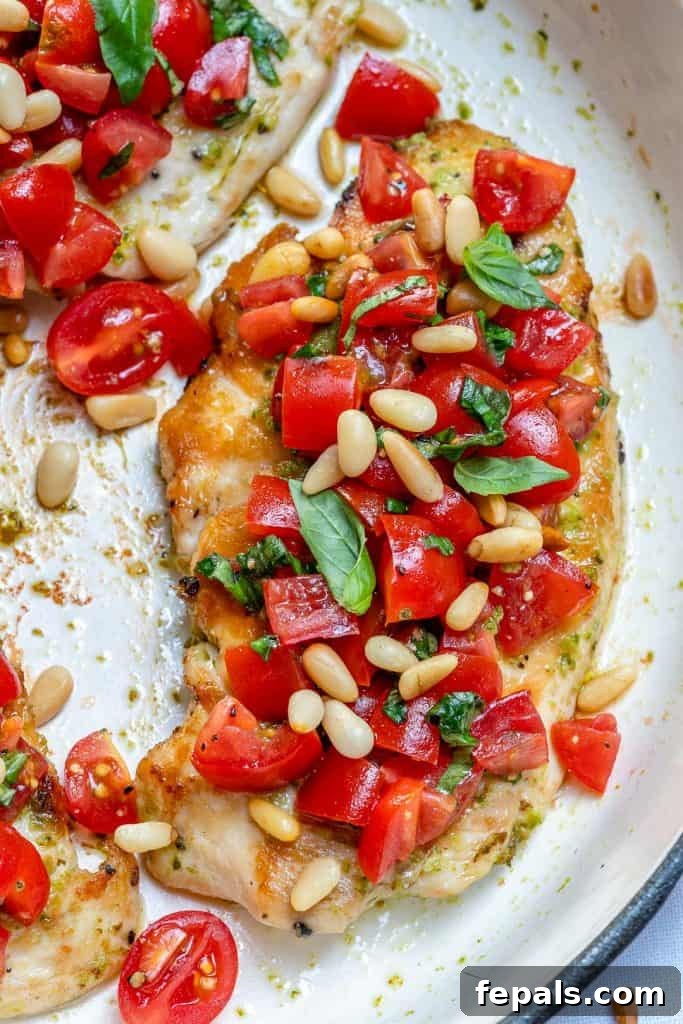 Top view of cooked Pesto grilled chicken breast topped with bruschetta toppings, including diced tomatoes and basil.