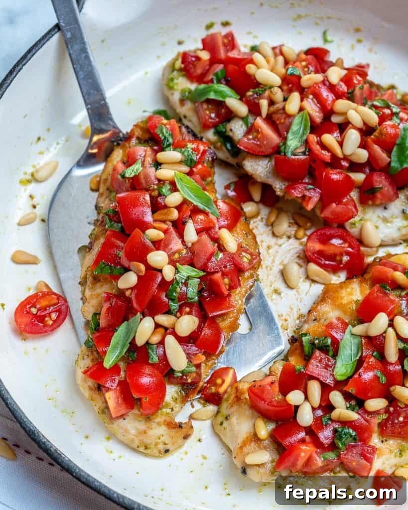 Spatula removing a Pesto bruschetta grilled chicken from pan, topped with tomatoes and pine nuts.
