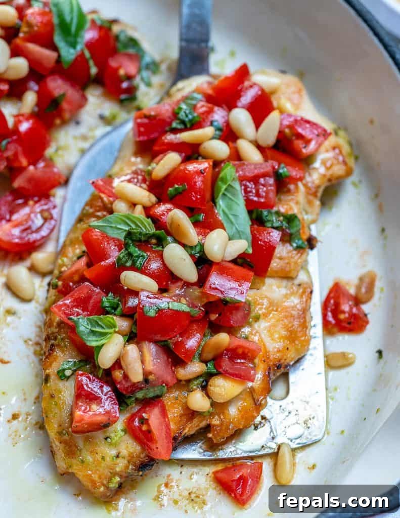 A top view of a single bruschetta grilled chicken on a pan topped with chopped tomatoes and pine nuts.