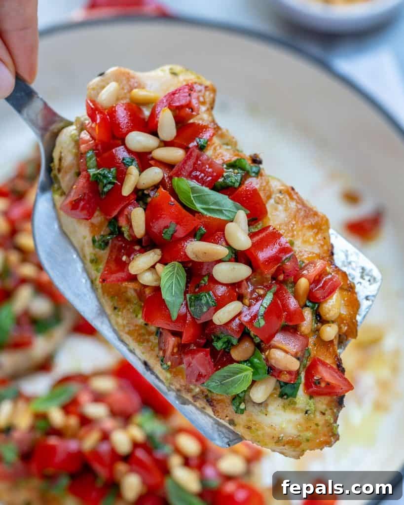 Spatula lifting a cooked chicken breast from pan topped with bruschetta tomato topping.