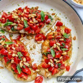 Top view of Pesto bruschetta chicken breasts in a skillet topped with chopped tomatoes