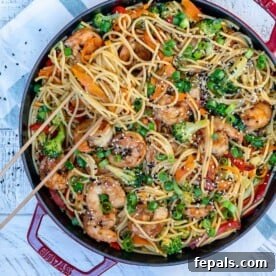 chopsticks in noodles and veggies in a red skillet.