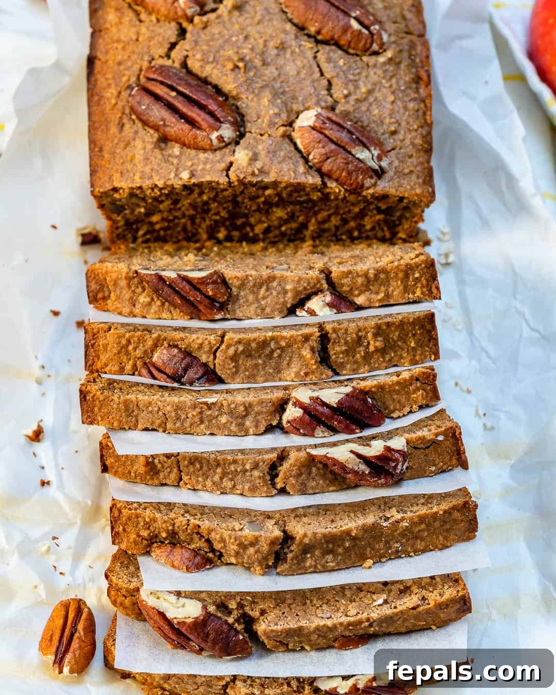 A beautiful loaf of brown apple cinnamon bread on a platter, with several slices cut and arranged.