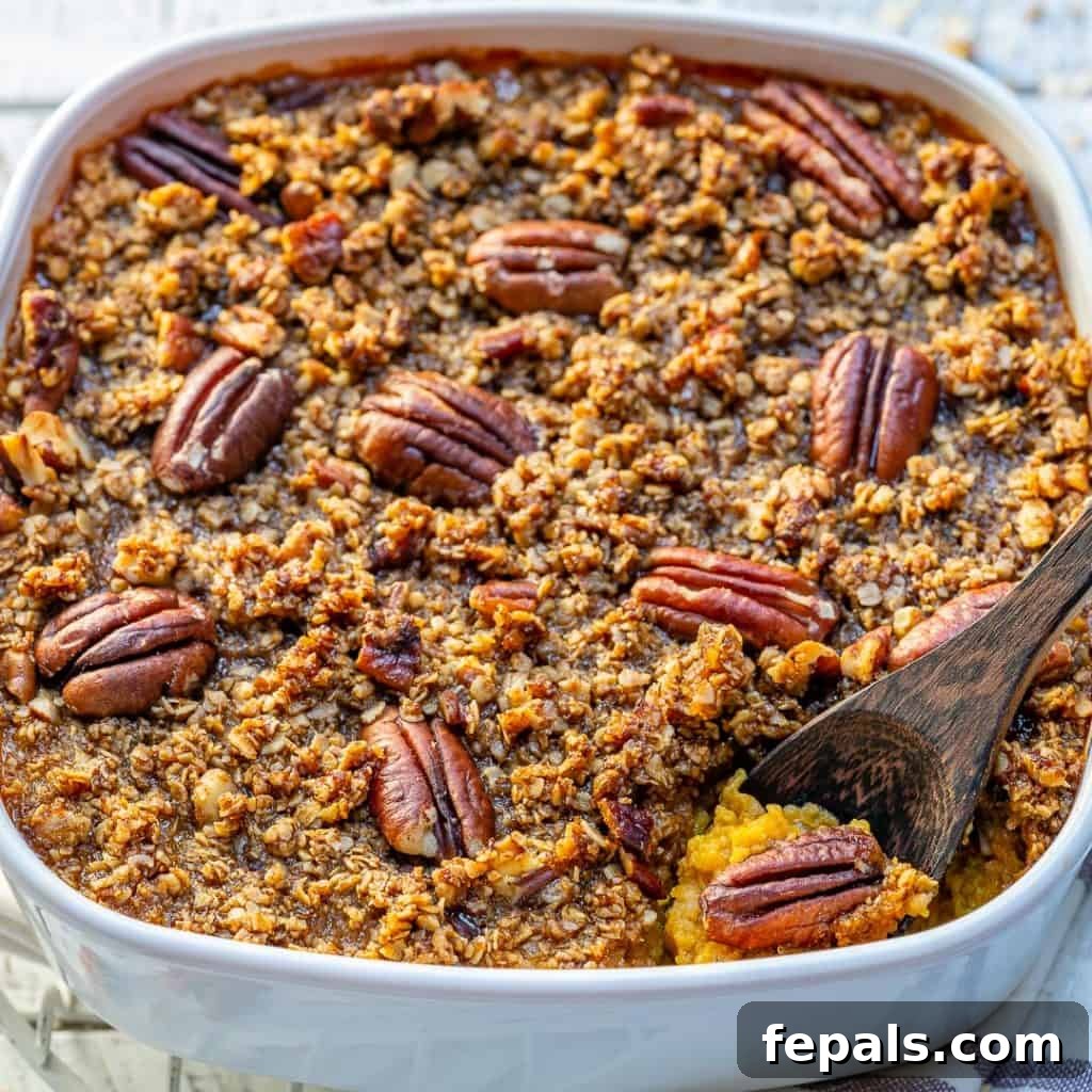 side shot of Butternut squash casserole in a white dish topped with sugar pecan and a wooden spoon in dish