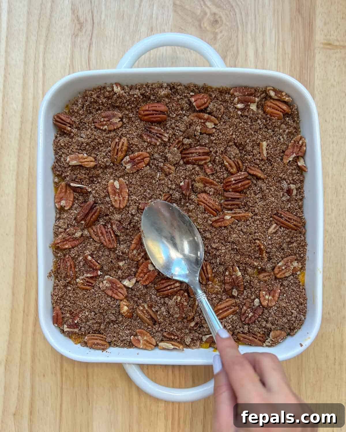Pecan and flour topping are added over the squash base in a dish.