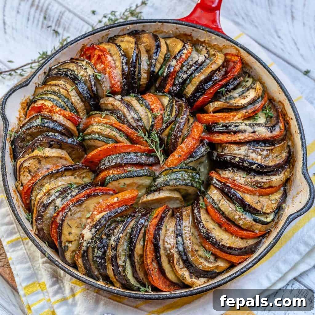 top view of a skillet with baked slices of eggplant, zucchini, and tomatoes stacked next to each other and topped with shredded parmesan chesse
