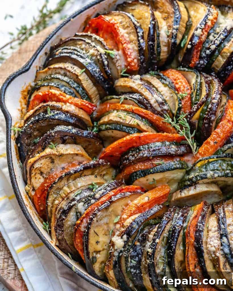 side shot of half a skillet of sliced zucchini, eggplants, and tomatoes and topped with parmesan cheese
