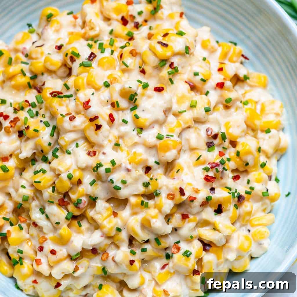 Velvety One-Pot Cheesy Corn 2 Top view of creamy, cheesy one-pot corn on a white plate, garnished with chili flakes and fresh chives.