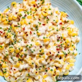 Top view of creamy, cheesy one-pot corn on a white plate, garnished with chili flakes and fresh chives.