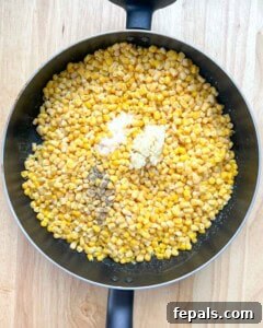 Velvety One-Pot Cheesy Corn 13 Corn was added to the pan, and salt, pepper, and minced garlic were added to it.