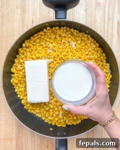 Velvety One-Pot Cheesy Corn 14 cheese and milk being added over the corn in the pan.