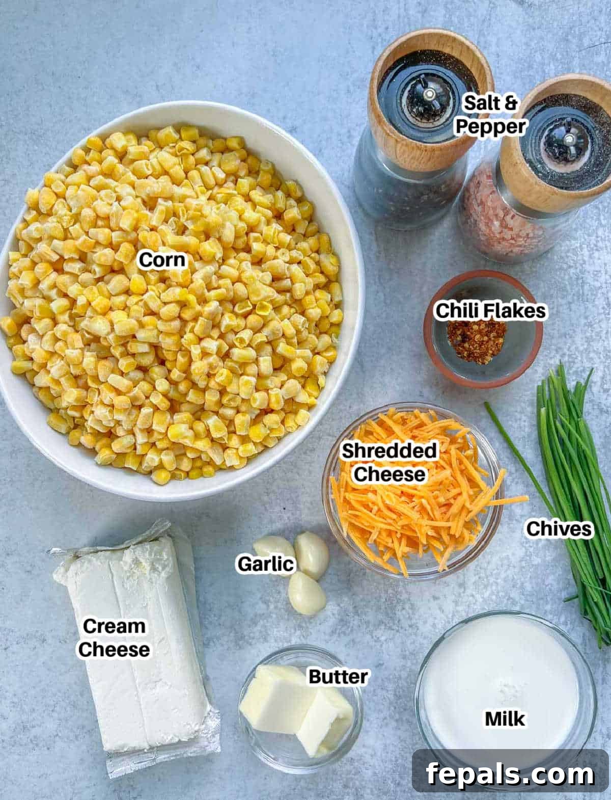 Velvety One-Pot Cheesy Corn 3 A vibrant display of fresh ingredients laid out on a cutting board, ready to make creamed corn, including corn kernels, butter, cream cheese, milk, shredded cheddar, garlic, and chives.
